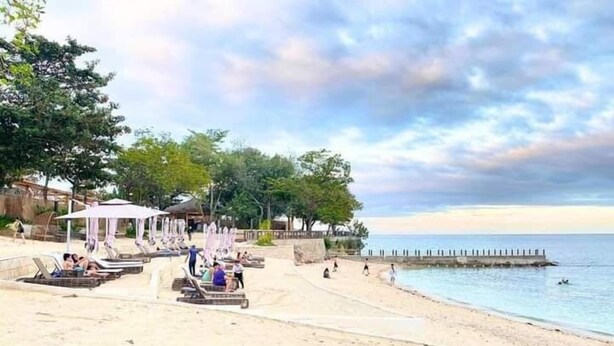 A beach with sun loungers and umbrellas, a wooden pier, and a clear sky.