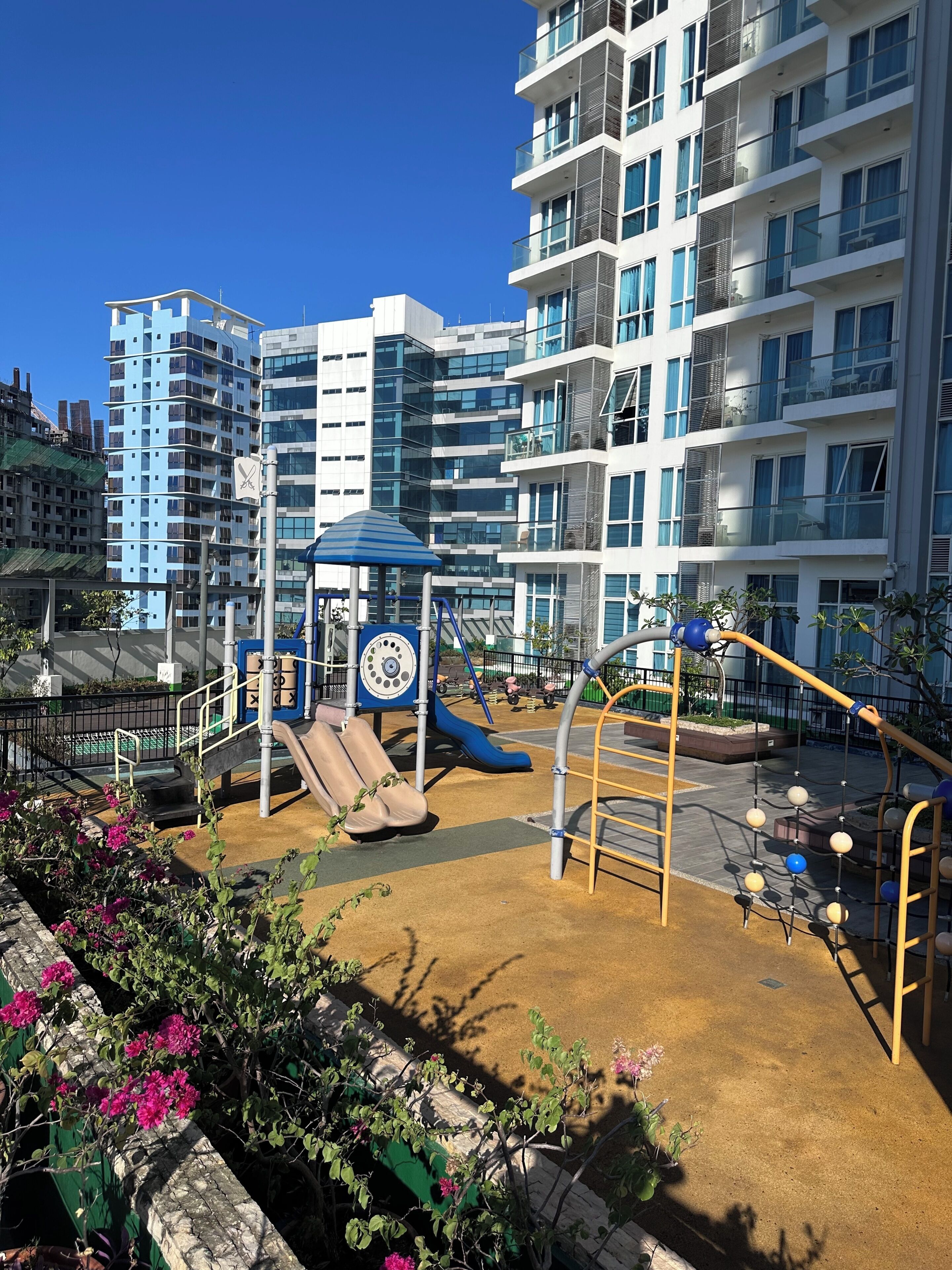 A playground with slides and climbing structures, surrounded by a building with multiple balconies and windows.