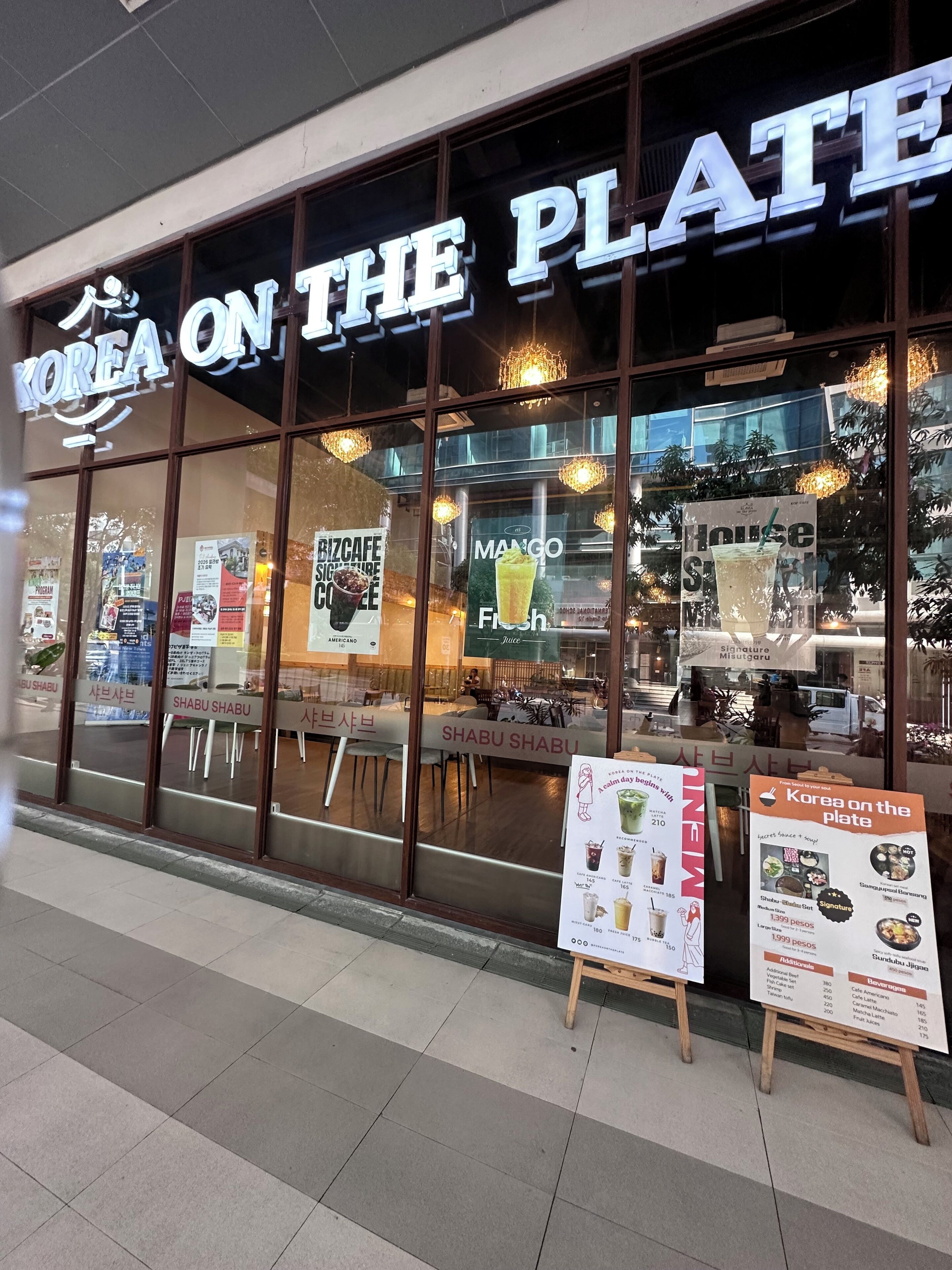 A restaurant named 'Korea on the Plate' with large glass windows, interior seating, and promotional posters.