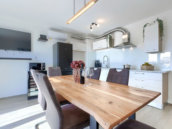 Une cuisine moderne avec des meubles blancs, une table à manger en bois et un four encastré.