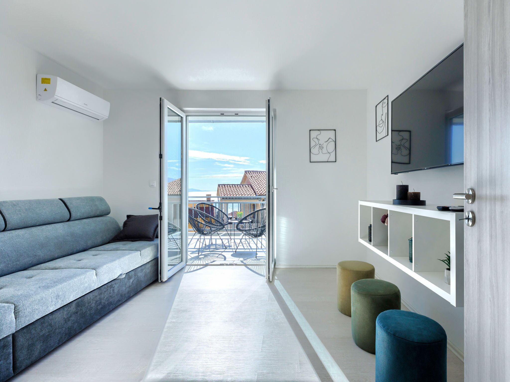 A modern living room with a grey sofa, a white console table, and a view of the outdoors through a glass door.