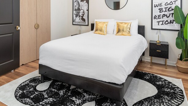 A modern bedroom with a large bed, a chandelier, a mirror, and artwork on the walls. - Taylor Swift Eras Inspired Home-10 min to Broadway Sleeps 10 (Nashville)