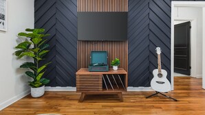 A room with a herringbone-patterned wall, a wooden console table with a record player, a guitar, and two potted plants. - Taylor Swift Eras Inspired Home-10 min to Broadway Sleeps 10 (Nashville)