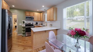 A modern kitchen with wooden cabinets, stainless steel appliances, and a glass dining table with pink chairs. - Taylor Swift Eras Inspired Home-10 min to Broadway Sleeps 10 (Nashville)