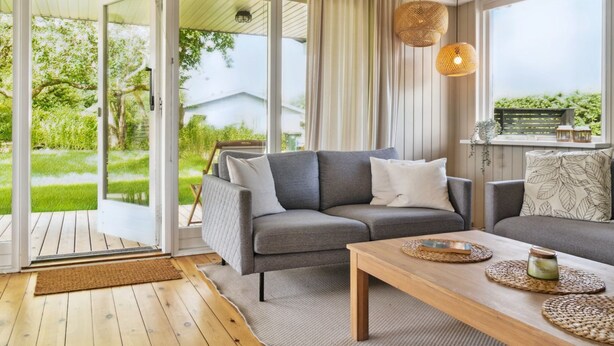 A modern living room with a grey sofa, a wooden coffee table, and a view of a garden through large sliding glass doors. - "Volmer" - 700m from the sea by Interhome (Hejls)