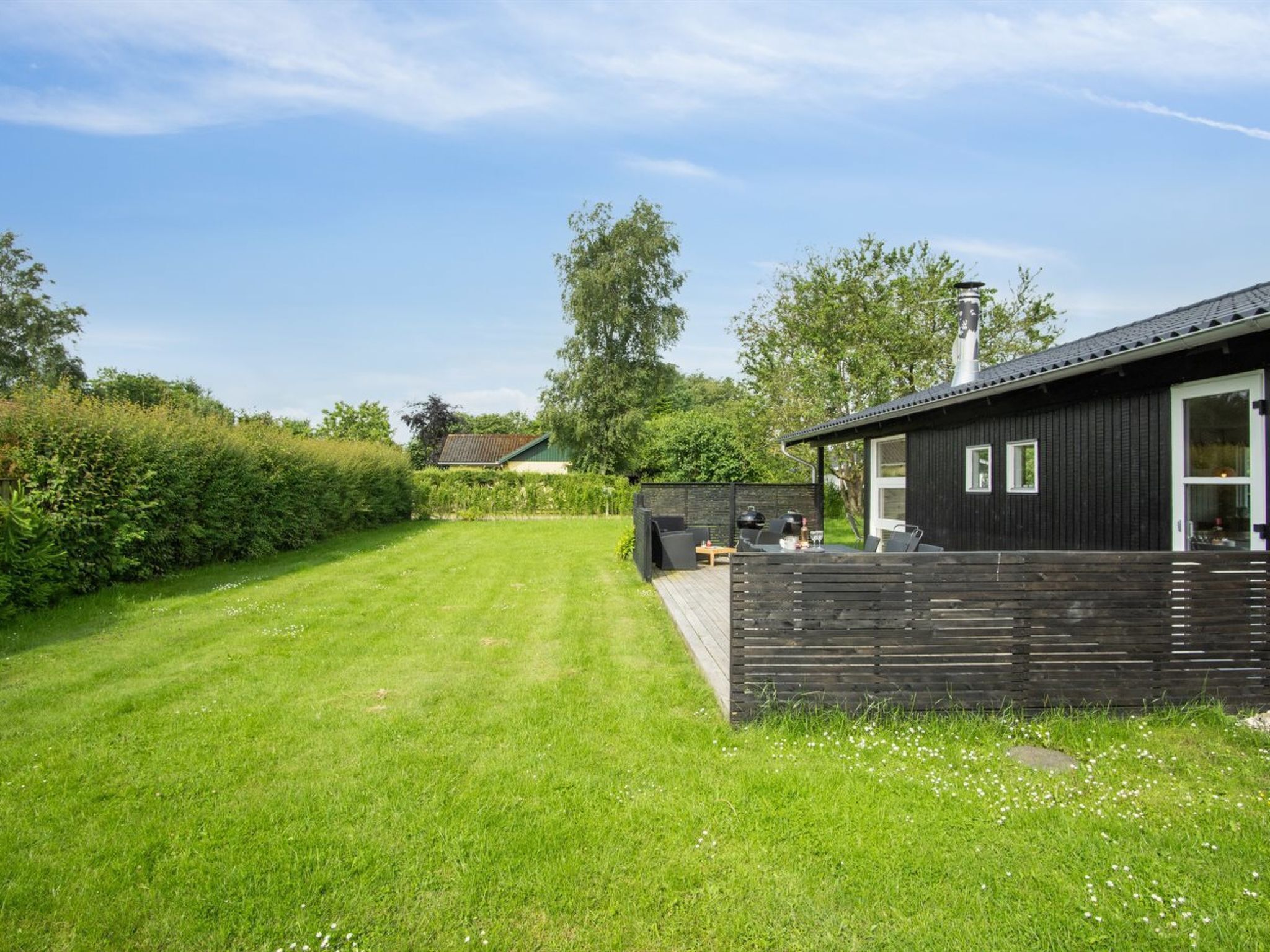 Une maison moderne dotée d’une terrasse, d’un espace barbecue et d’une pelouse bien entretenue.