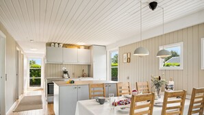 A modern kitchen with white cabinets, a wooden island, and a dining area with a white table and wooden chairs. - "Volmer" - 700m from the sea by Interhome (Hejls)