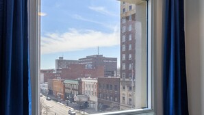 Vista desde una ventana con cortinas azules, que da a una calle con varios edificios, incluyendo un edificio de ladrillo con el letrero "Kentucky Utilities Company".