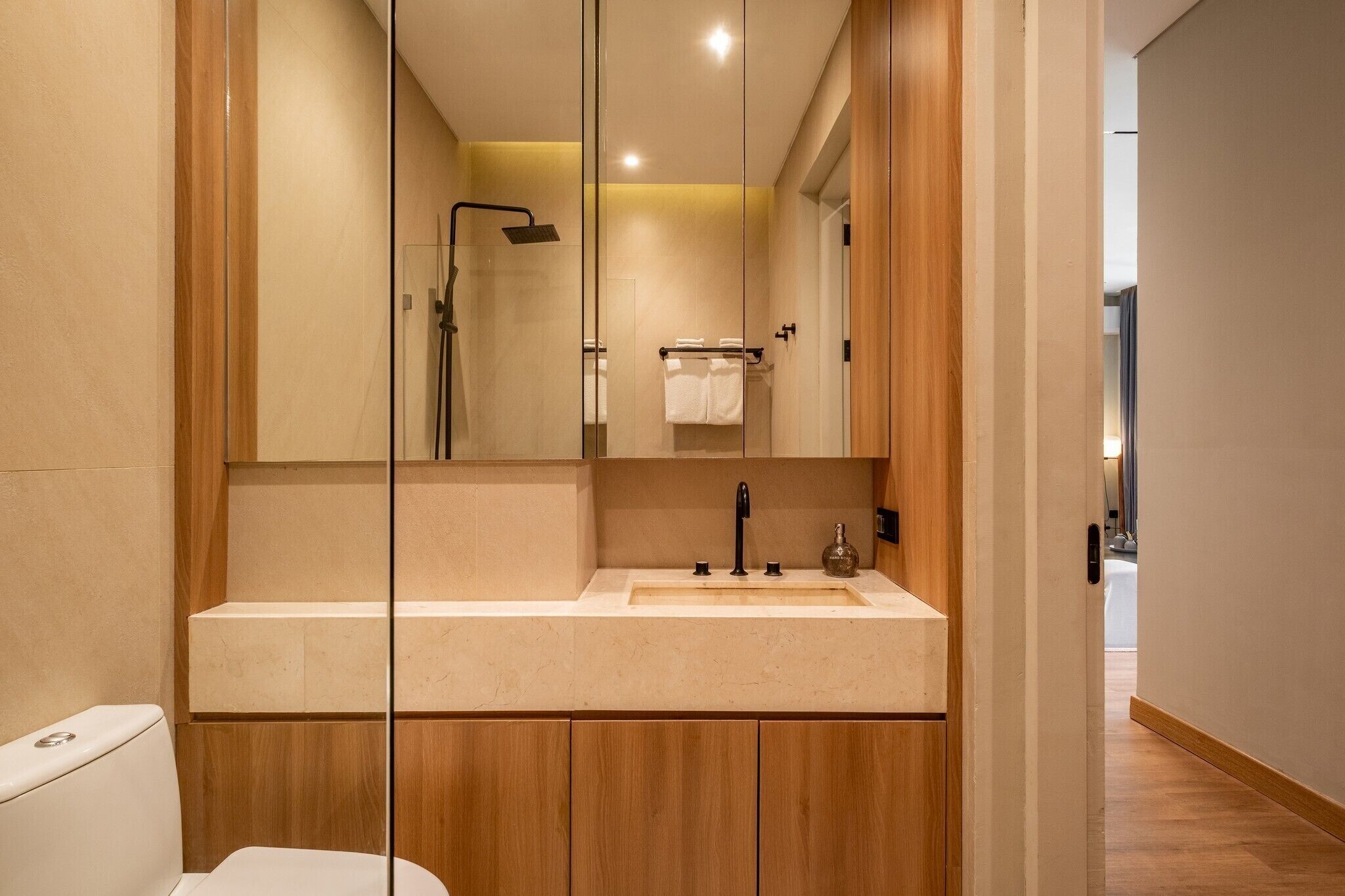 Een moderne badkamer met een glazen douchecabine, een houten wastafelmeubel en een grote spiegel.