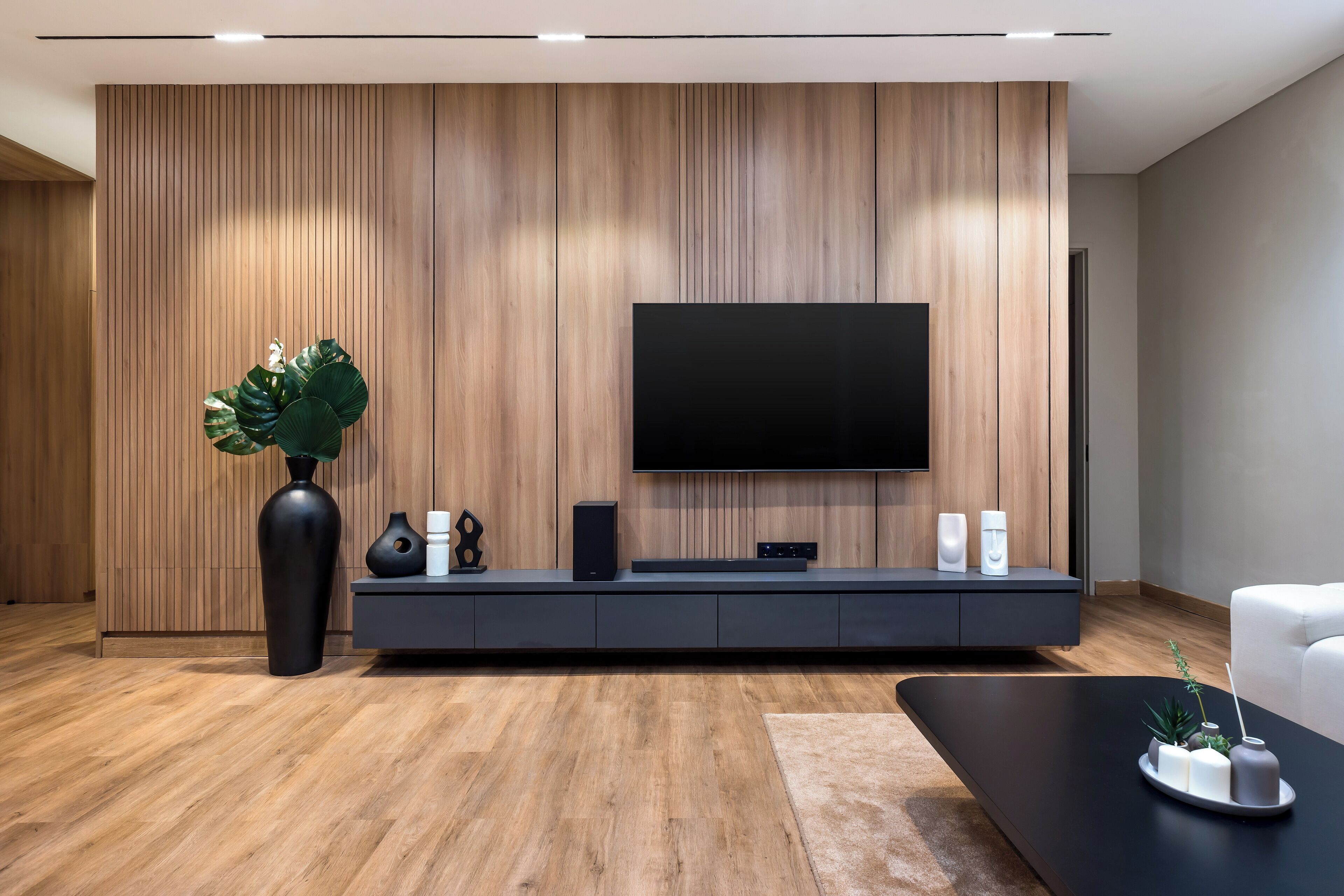 A modern living room with a wooden panel wall, a large flat-screen TV, a black entertainment unit, and a white sofa.