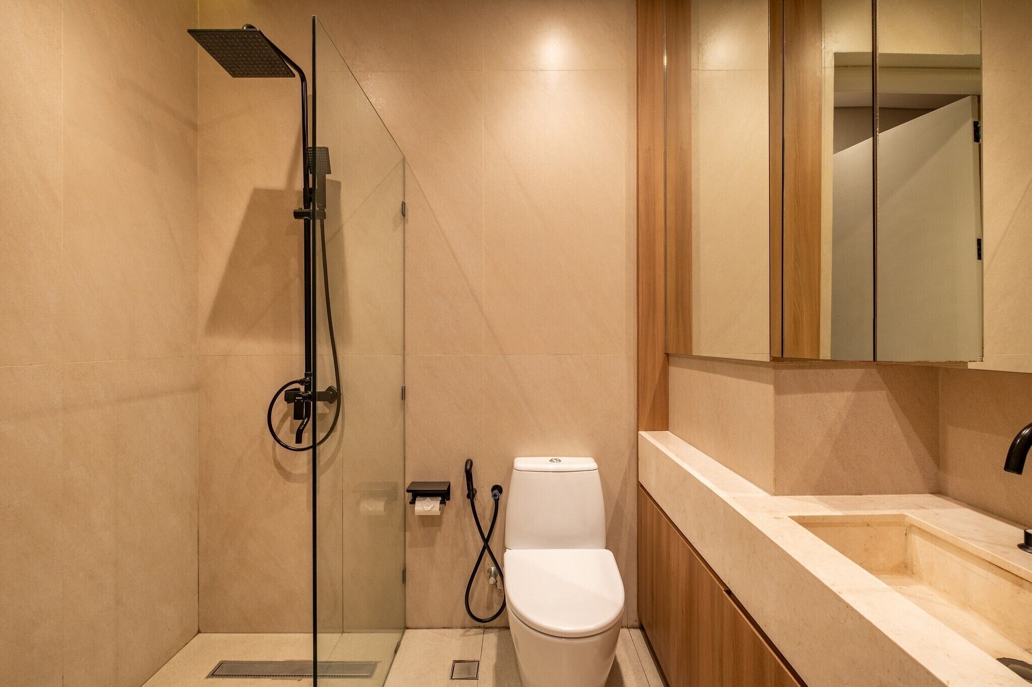Un baño moderno con ducha envuelta en vidrio, inodoro y lavamanos con espejo superior.