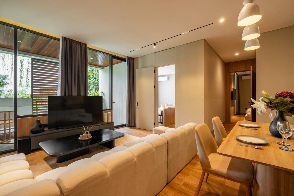Una sala de estar moderna con un televisor de pantalla plana grande, un sofá, una mesa de comedor con sillas y un jarrón con flores.
