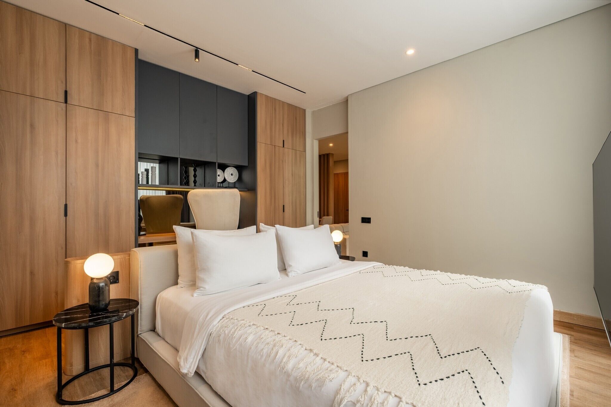 Une chambre moderne avec un grand lit, une armoire en bois et une petite table avec une lampe.