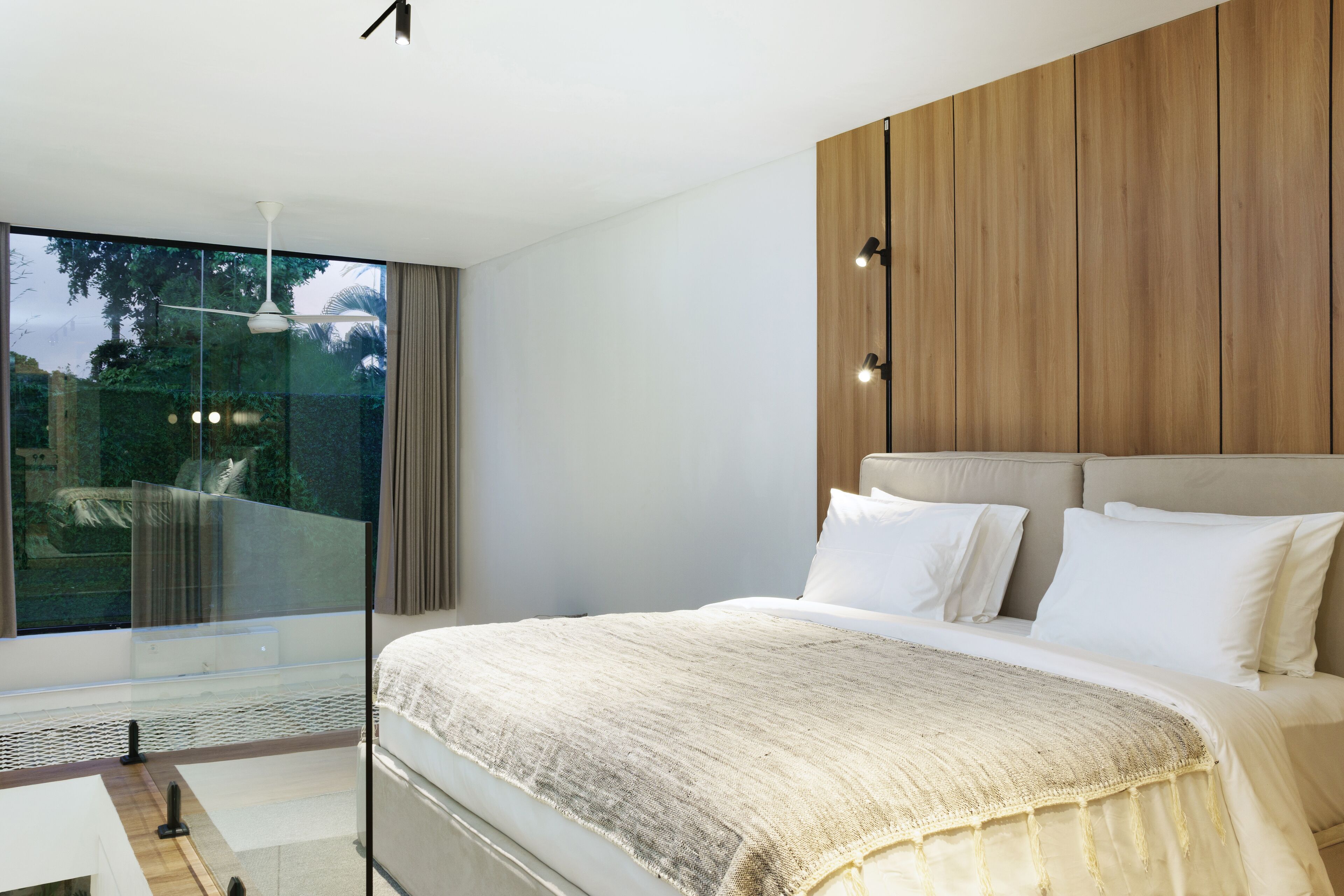 A modern bedroom with a large bed, a wooden panel wall, and a glass door leading to a balcony.