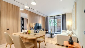 Ein modernes Wohnzimmer mit einem Holzespeisetisch, beigen Sesseln, einer Couch und einem Fernseher.