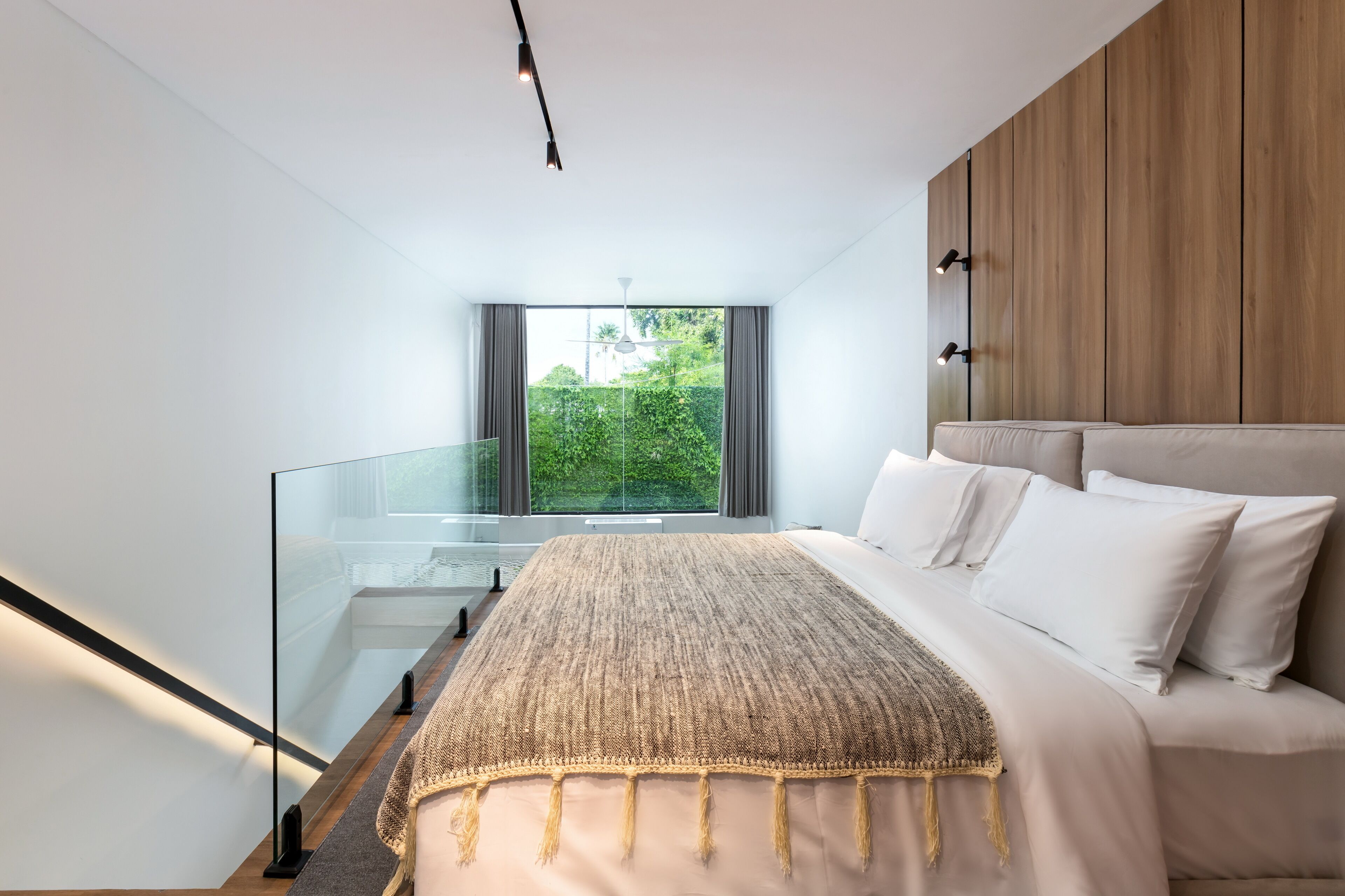 Un dormitorio con una cama grande, barandilla de vidrio y vistas al exterior.