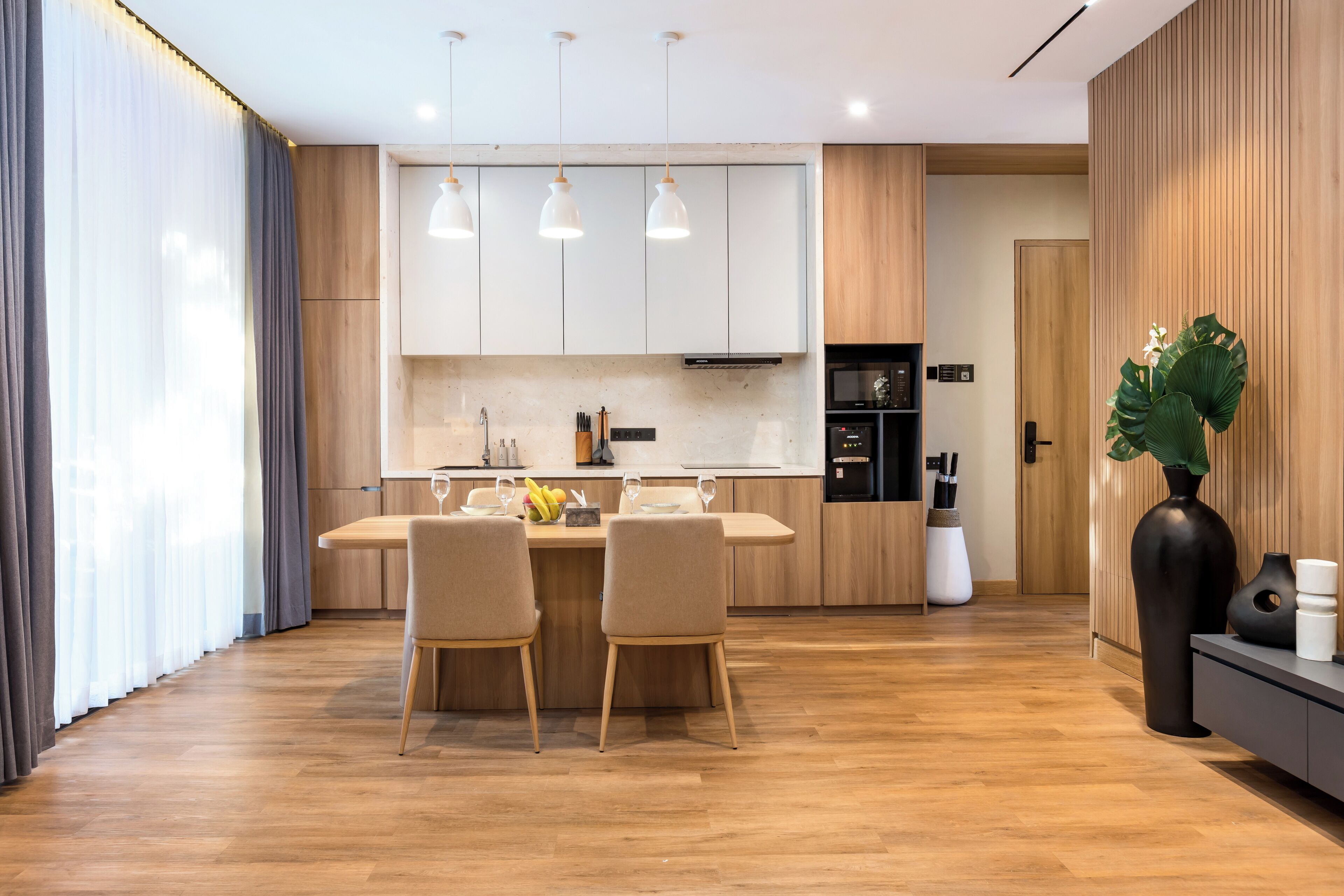 A modern kitchen with wooden cabinets, a dining area with two chairs, and a large plant.