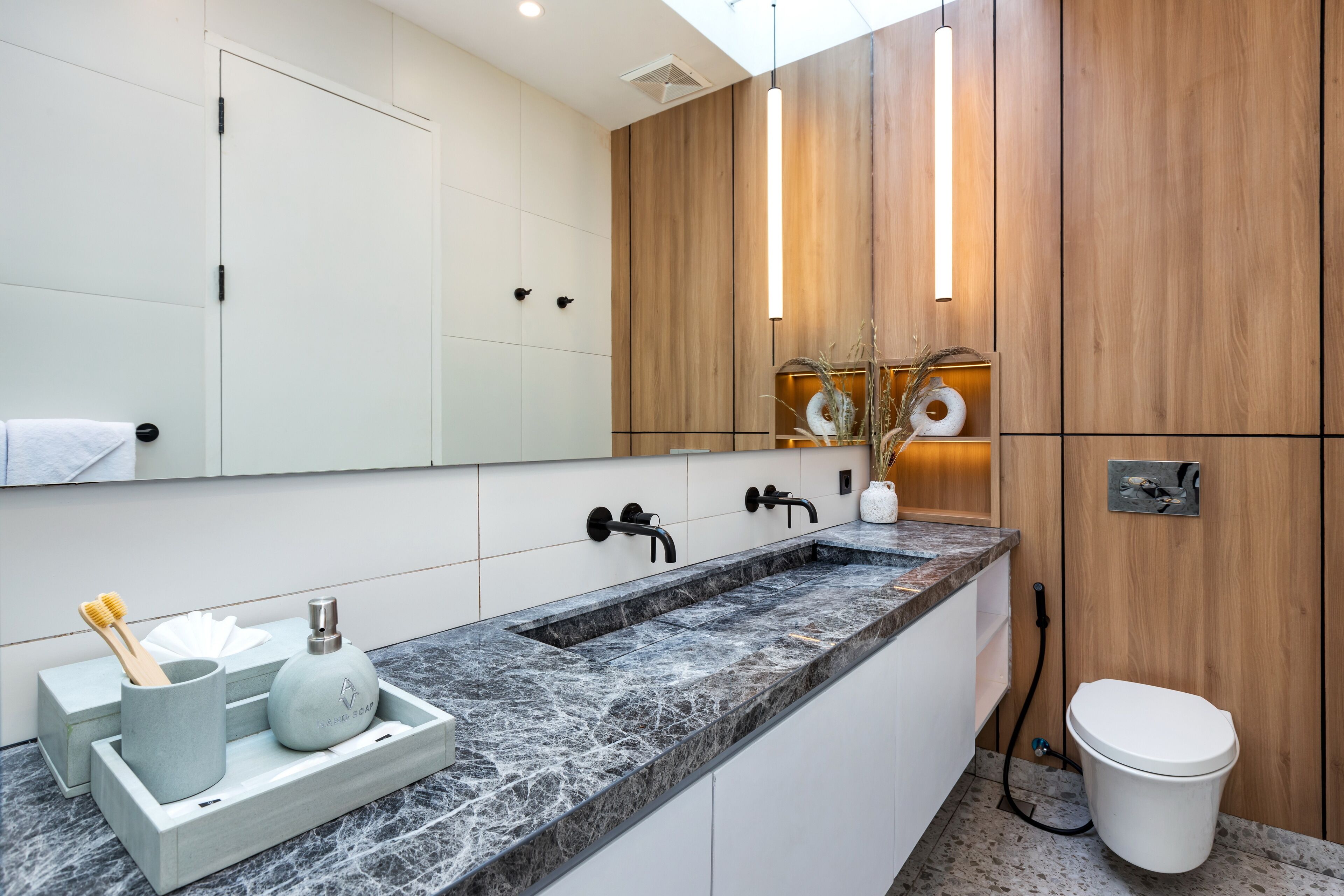 Un baño moderno con lavamanos de mármol, armarios de madera y un espejo grande.