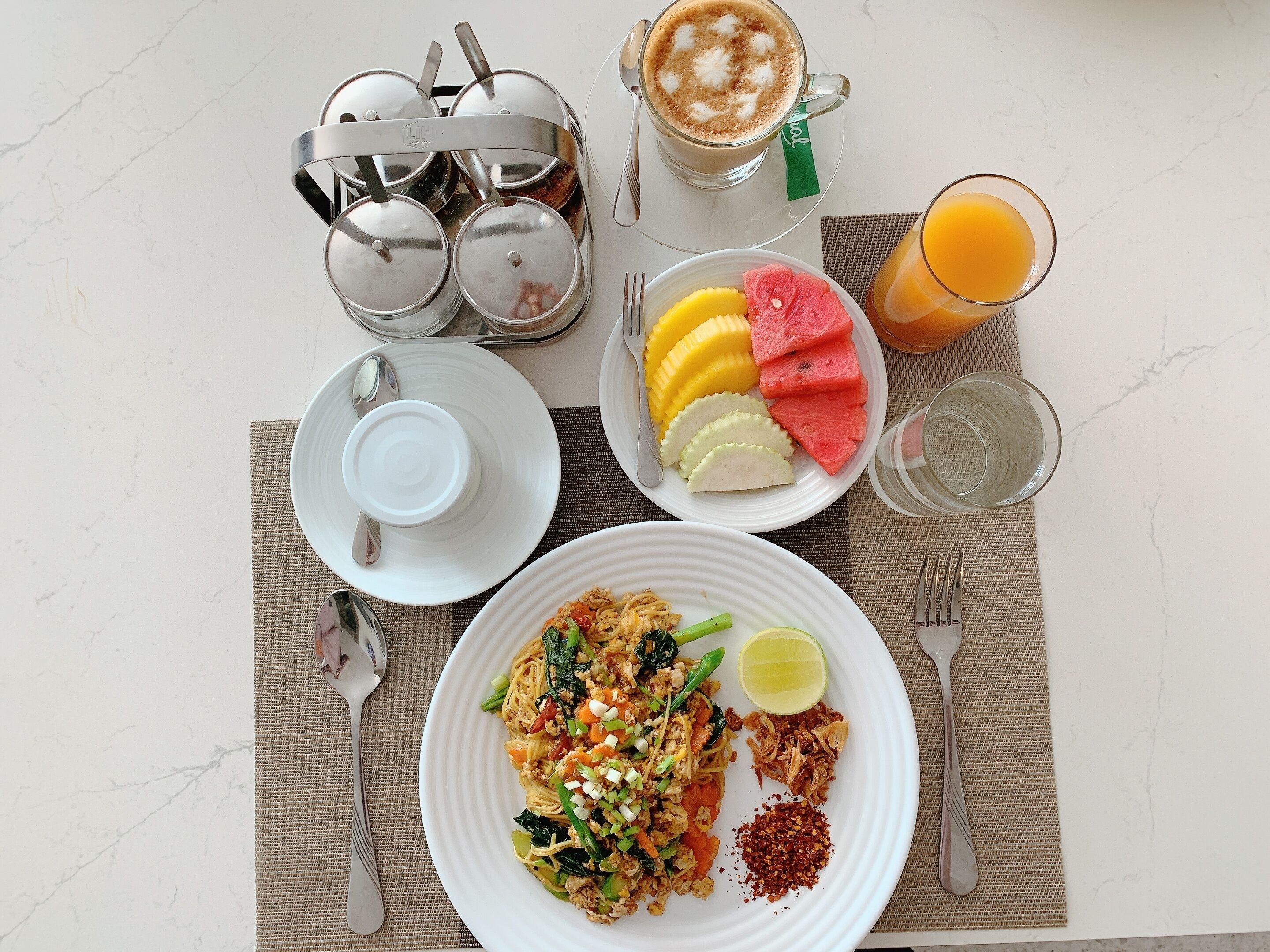 A breakfast setting with a plate of noodles, fruit, and a cup of coffee.