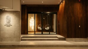 A hotel entrance with a modern design, featuring a logo on the wall, a staircase leading to the entrance, and two hanging chairs outside. - SN Residences (Vientiane)