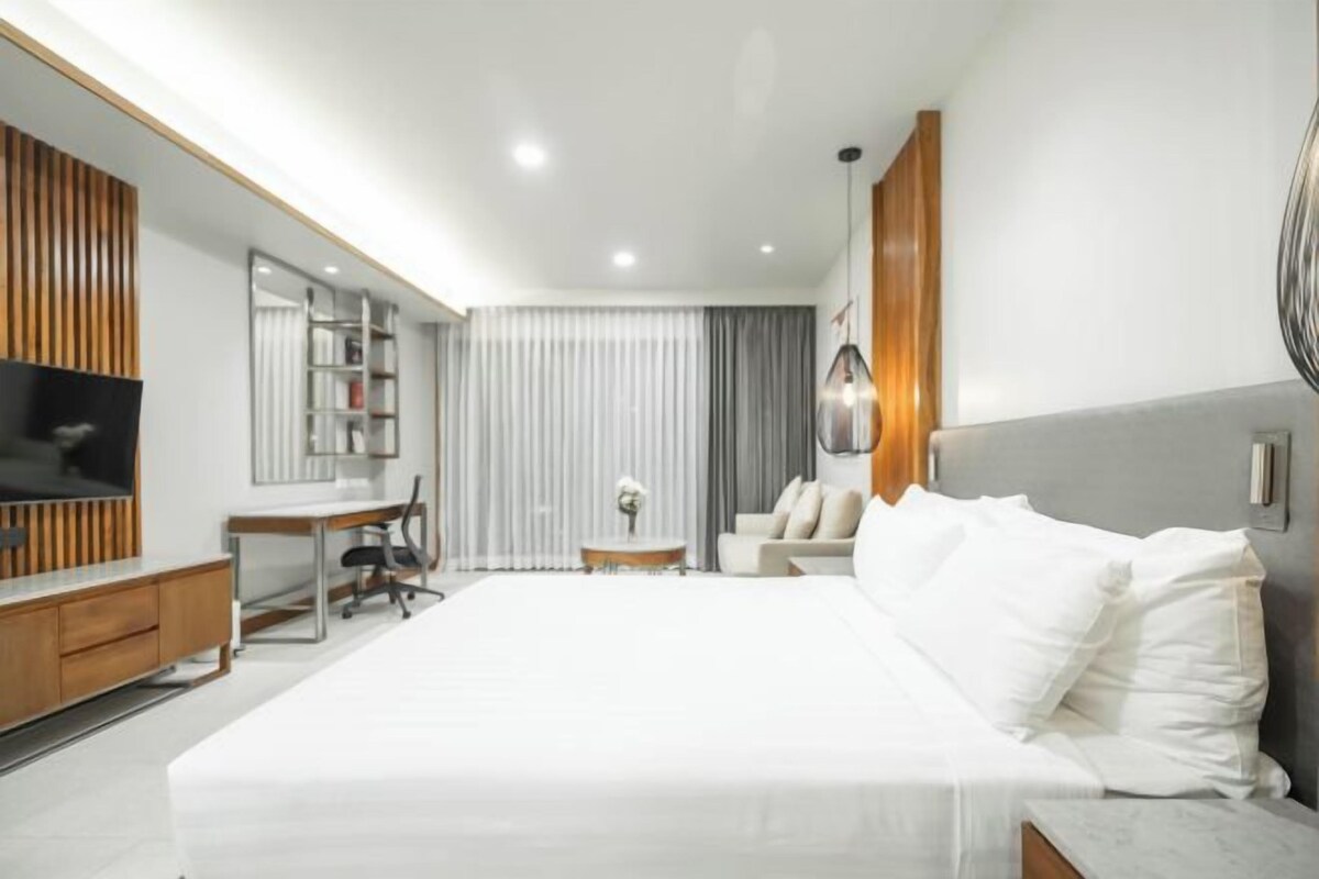 A modern hotel room with a large bed, a desk, a TV, and a seating area.