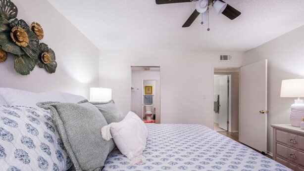 A bedroom with a bed, bedside tables, a ceiling fan, and a bathroom visible through an open door. - Heart of Homewood and Minutes from Birmingham (Birmingham)