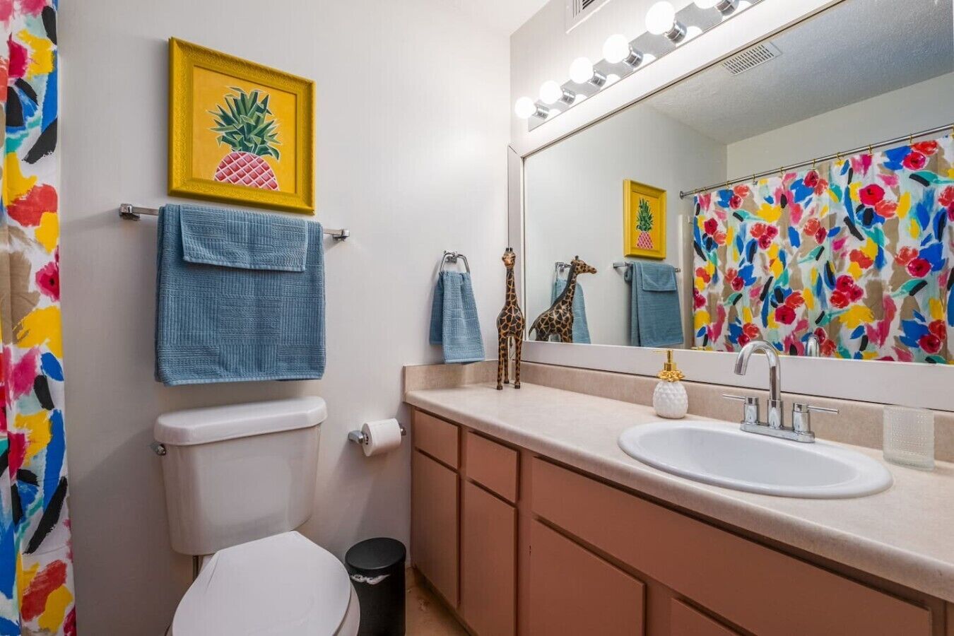 A bathroom with a toilet, a sink, a mirror with lights, and a towel rack.