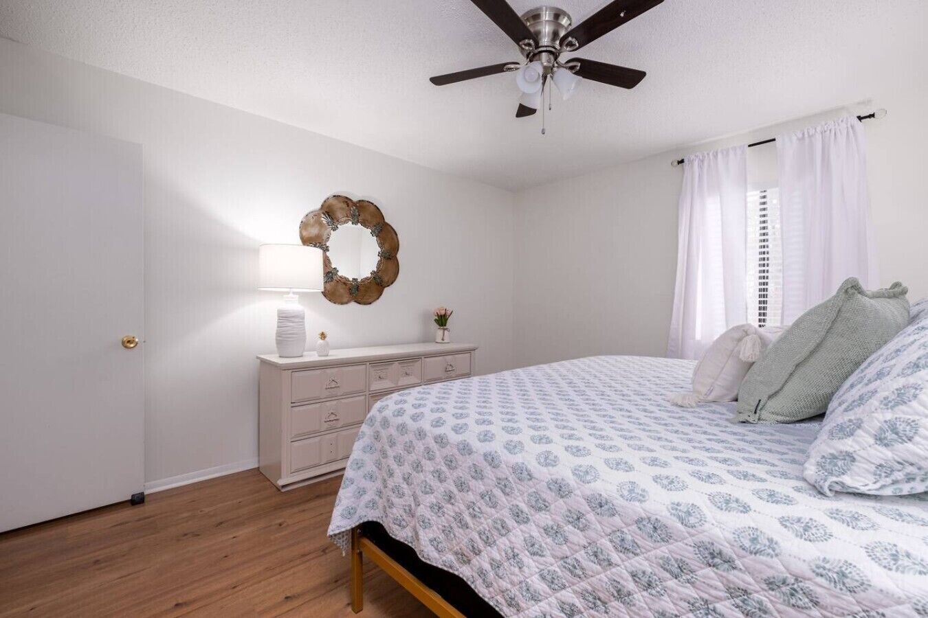 Un dormitorio con cama, cómoda, ventilador de techo y un espejo decorativo.