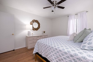 A bedroom with a bed, a dresser, a ceiling fan, and a decorative mirror.