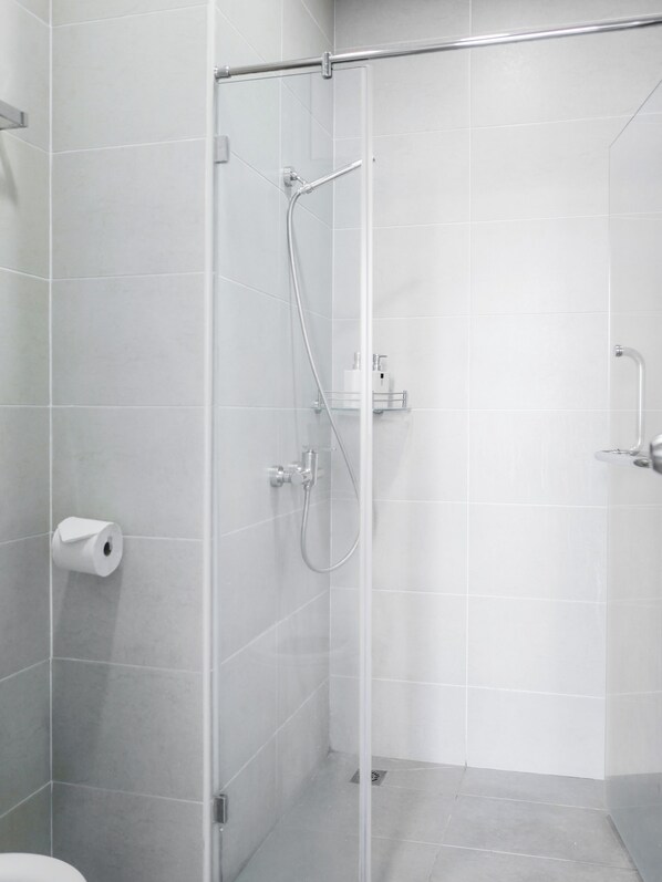 Una ducha moderna con mampara de vidrio, ducha de mano y soporte para papel higiénico en la pared.