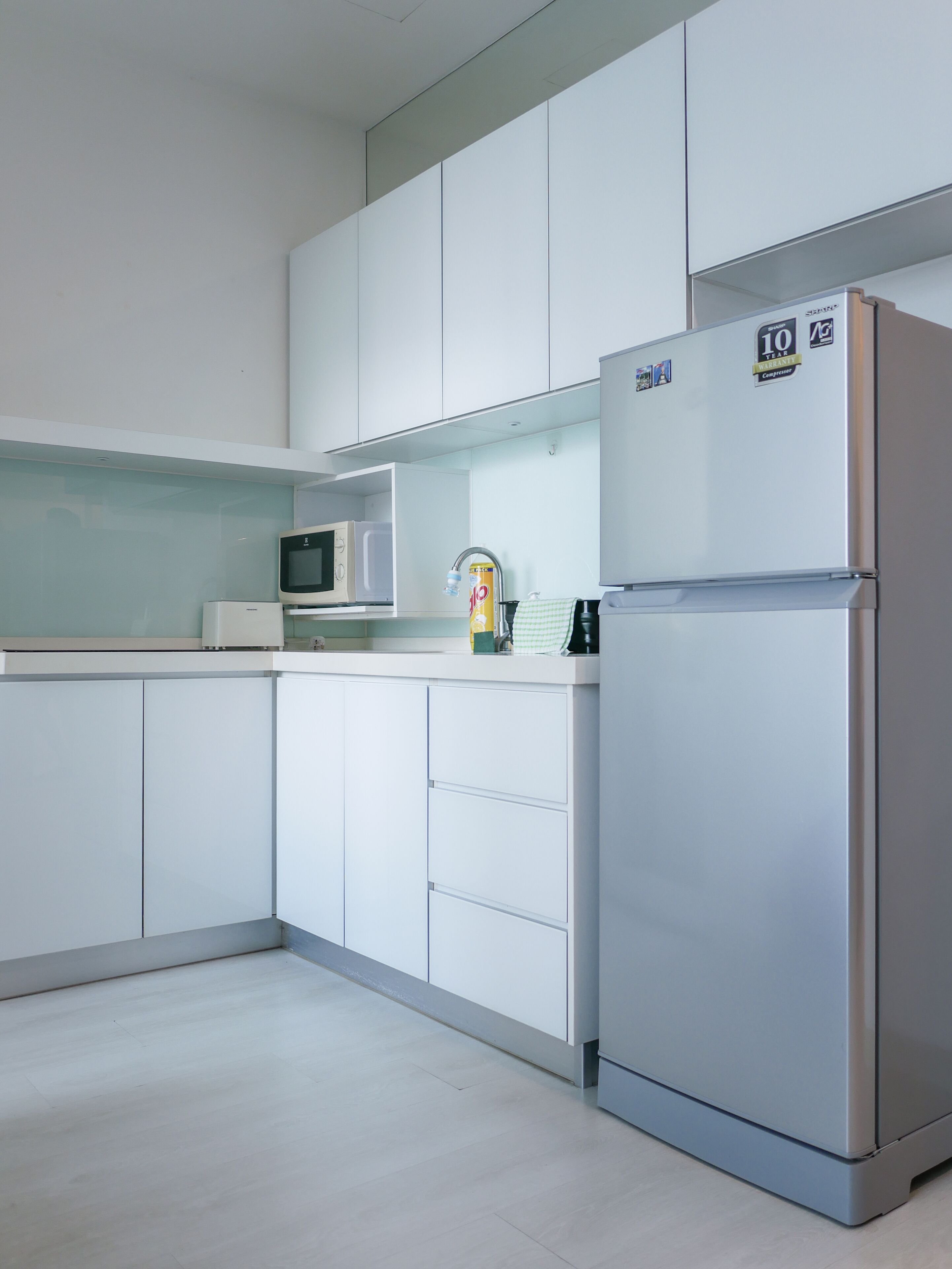 A modern kitchen with white cabinets, a stainless steel refrigerator, a microwave, and a kettle.