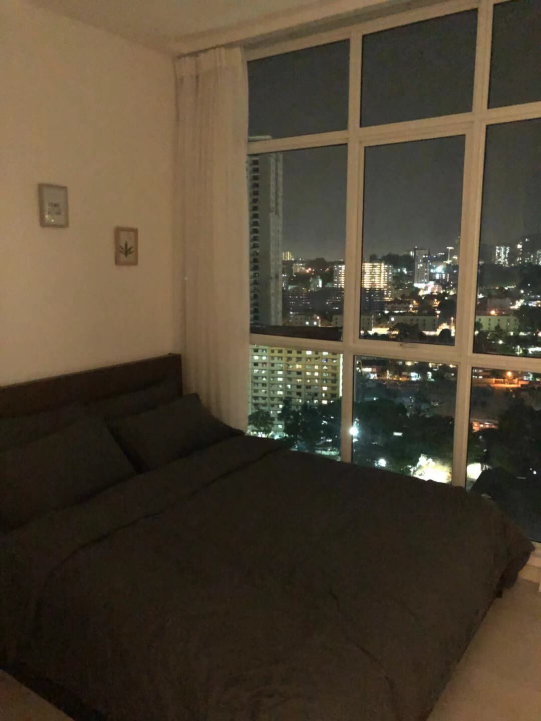 A bedroom with a large bed, a window with a city view at night, and two small wall decorations.