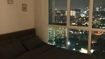 A bedroom with a large bed, a window with a city view at night, and two small wall decorations.