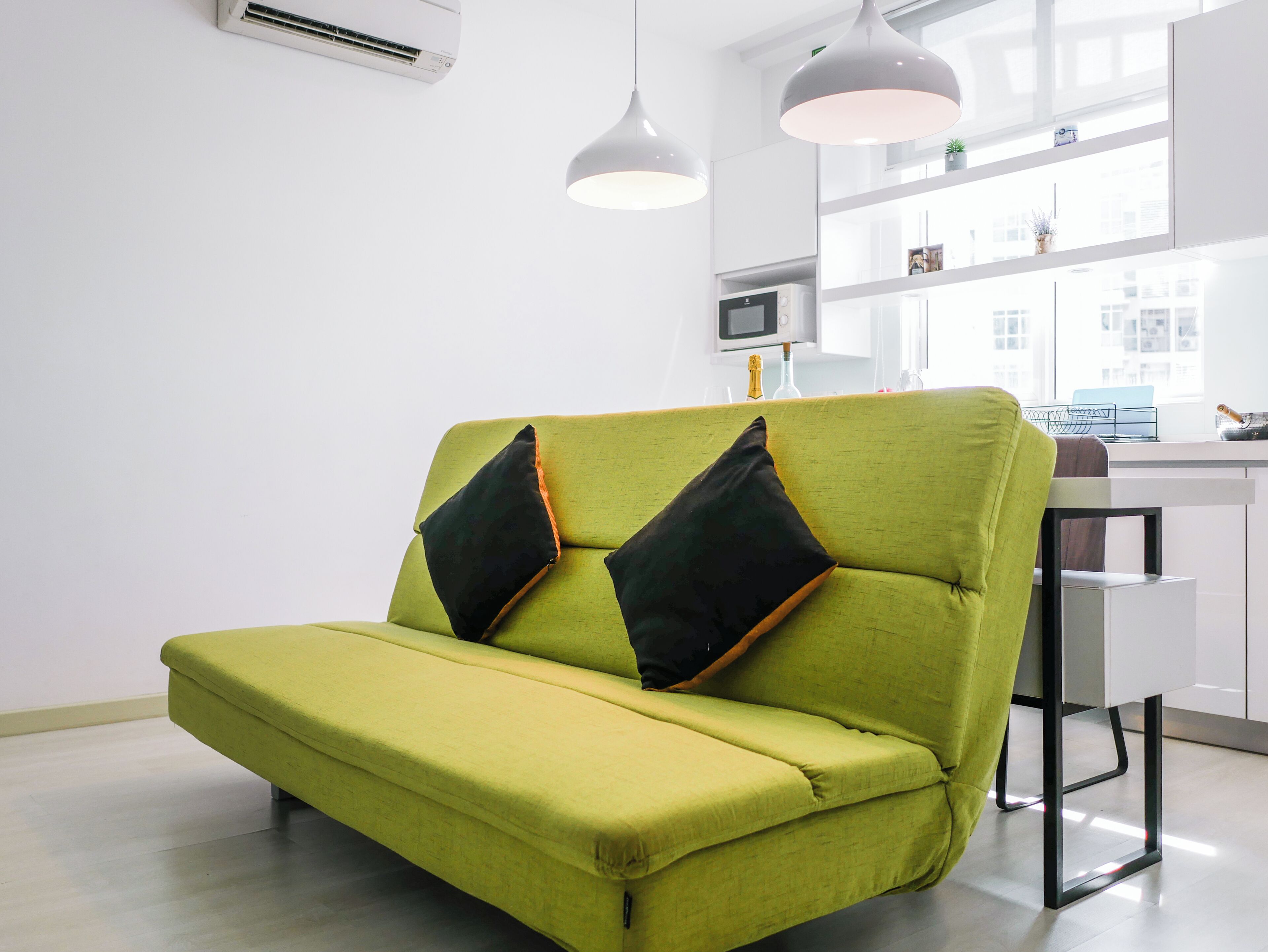 Ein grünes Sofa mit schwarzen Kissen in einem modernen, hell einfallenden Raum mit weißen Wänden und einem großen Fenster.