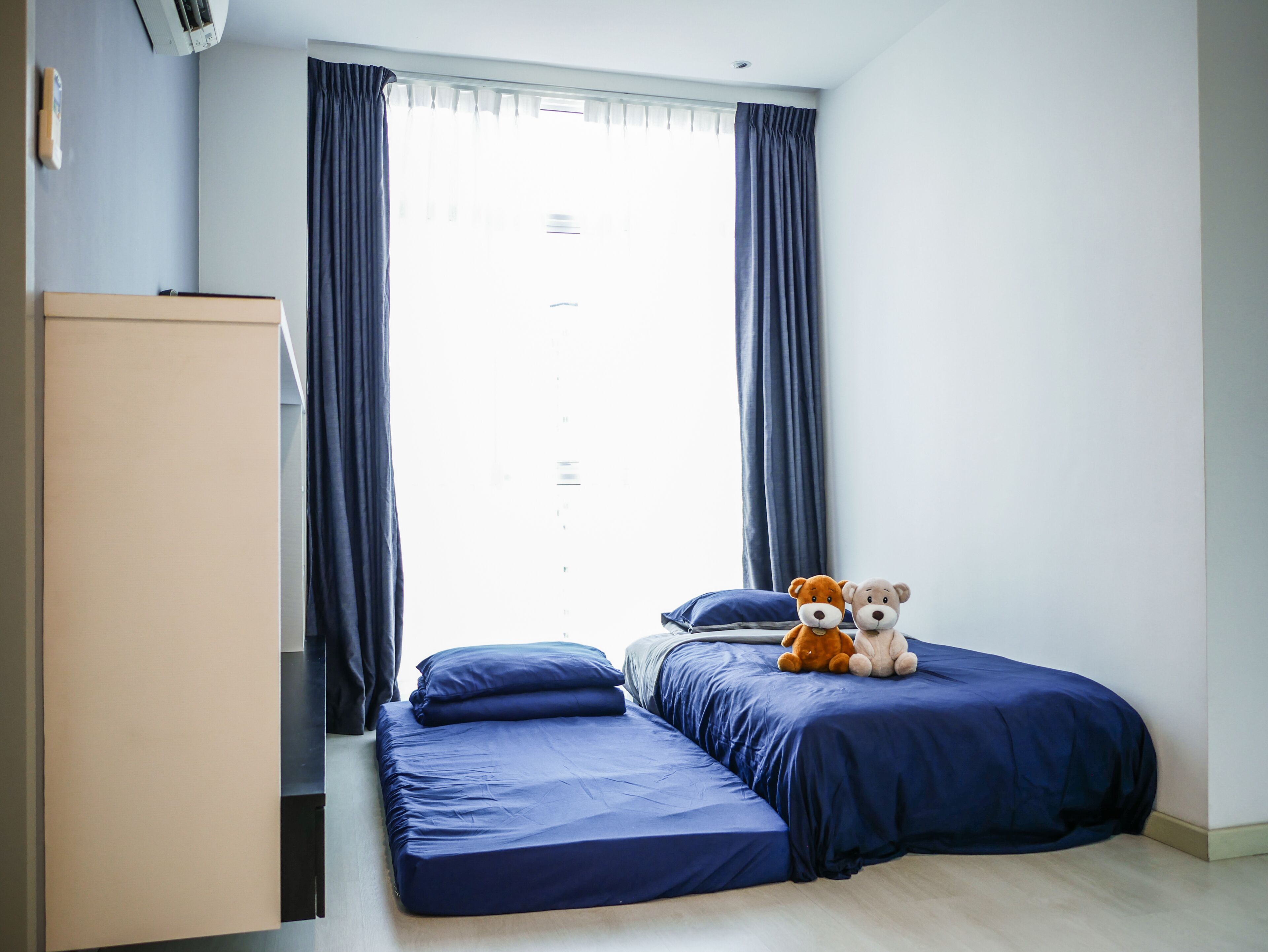 Un dormitorio con cama, dos almohadas, un armario y una ventana con cortinas.