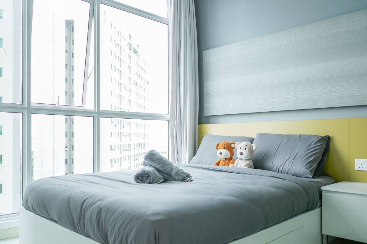 A modern bedroom with a large window, a neatly made bed, and two plush toys on the pillows.