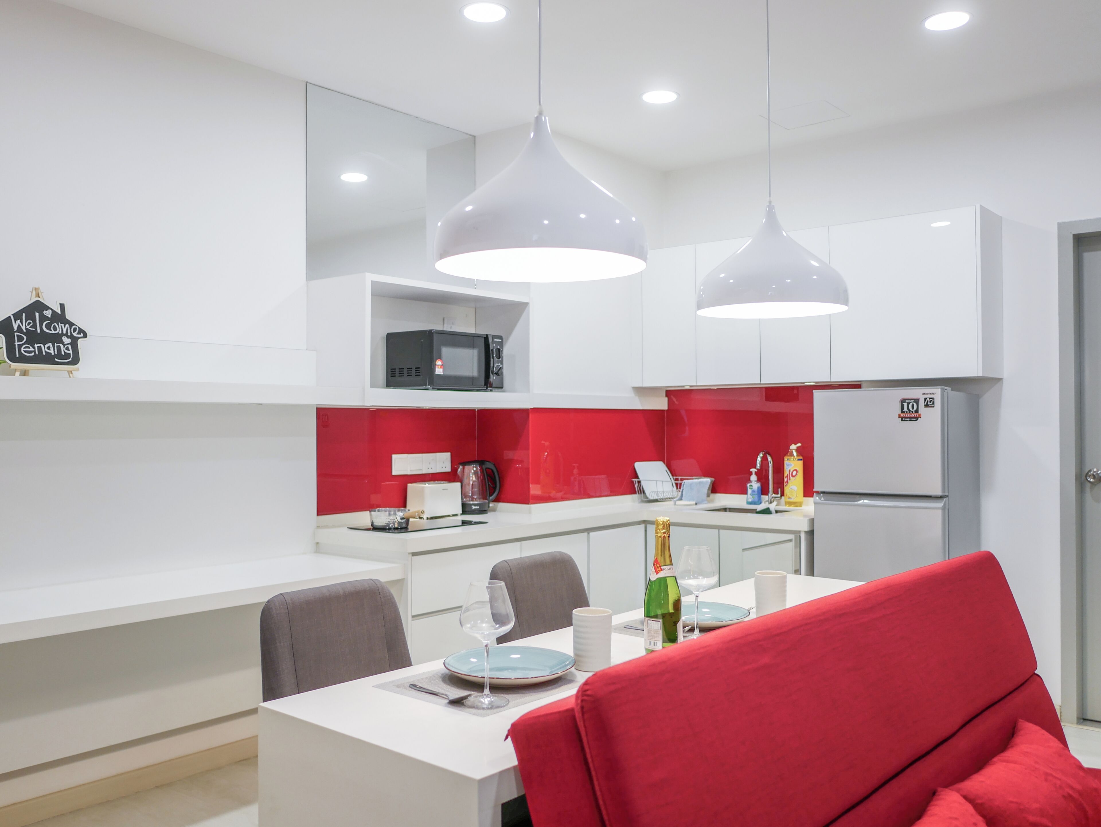 A modern kitchen with white cabinets, a red backsplash, and a dining area with a red chair.