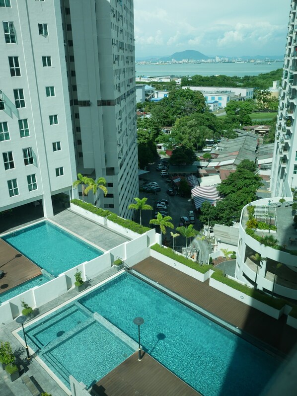 A high-rise building with a rooftop pool area, surrounded by greenery and a view of the cityscape.