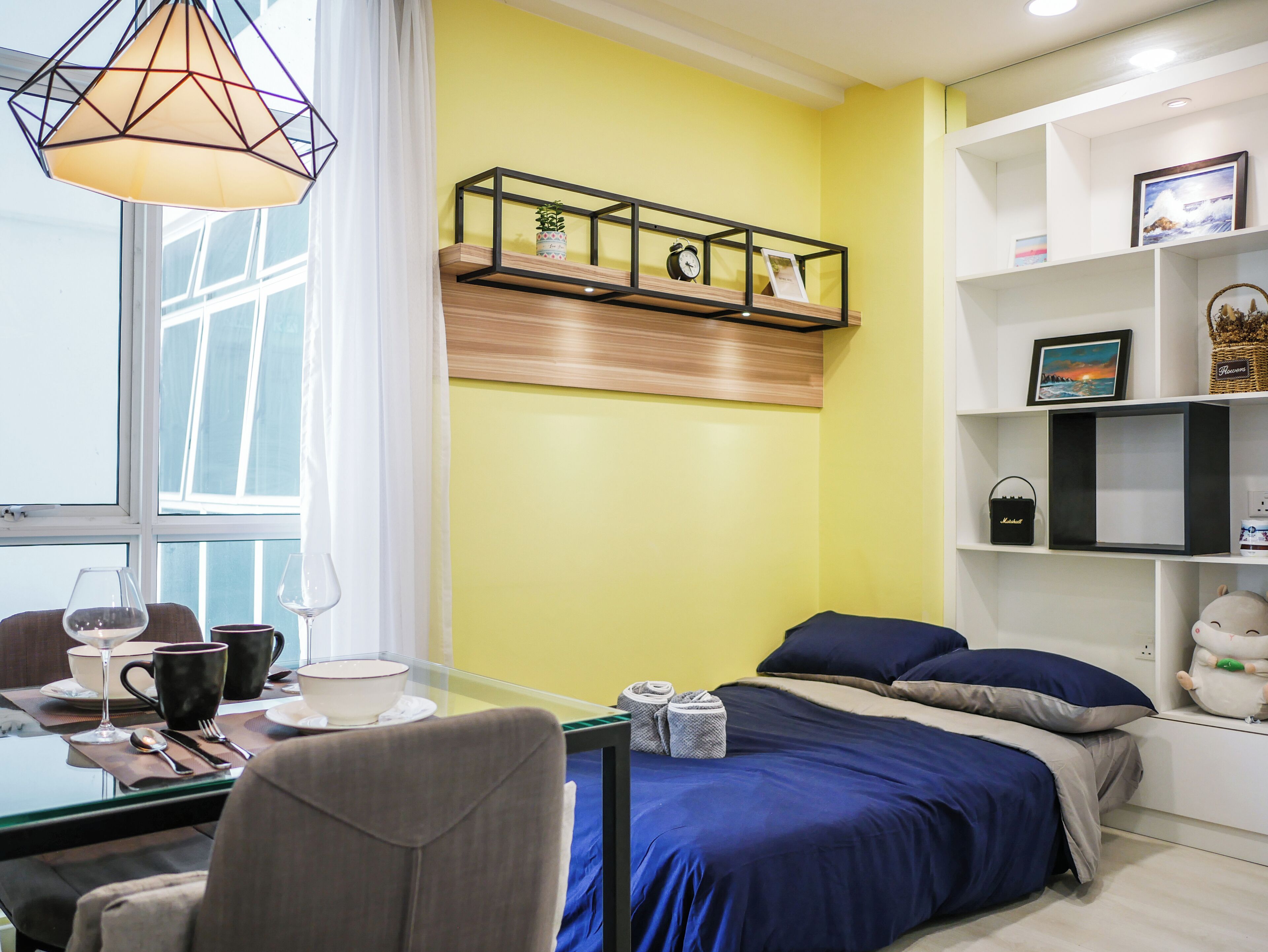 Une chambre moderne comprenant un lit, une table à manger avec des chaises et une étagère ornée d’objets décoratifs.