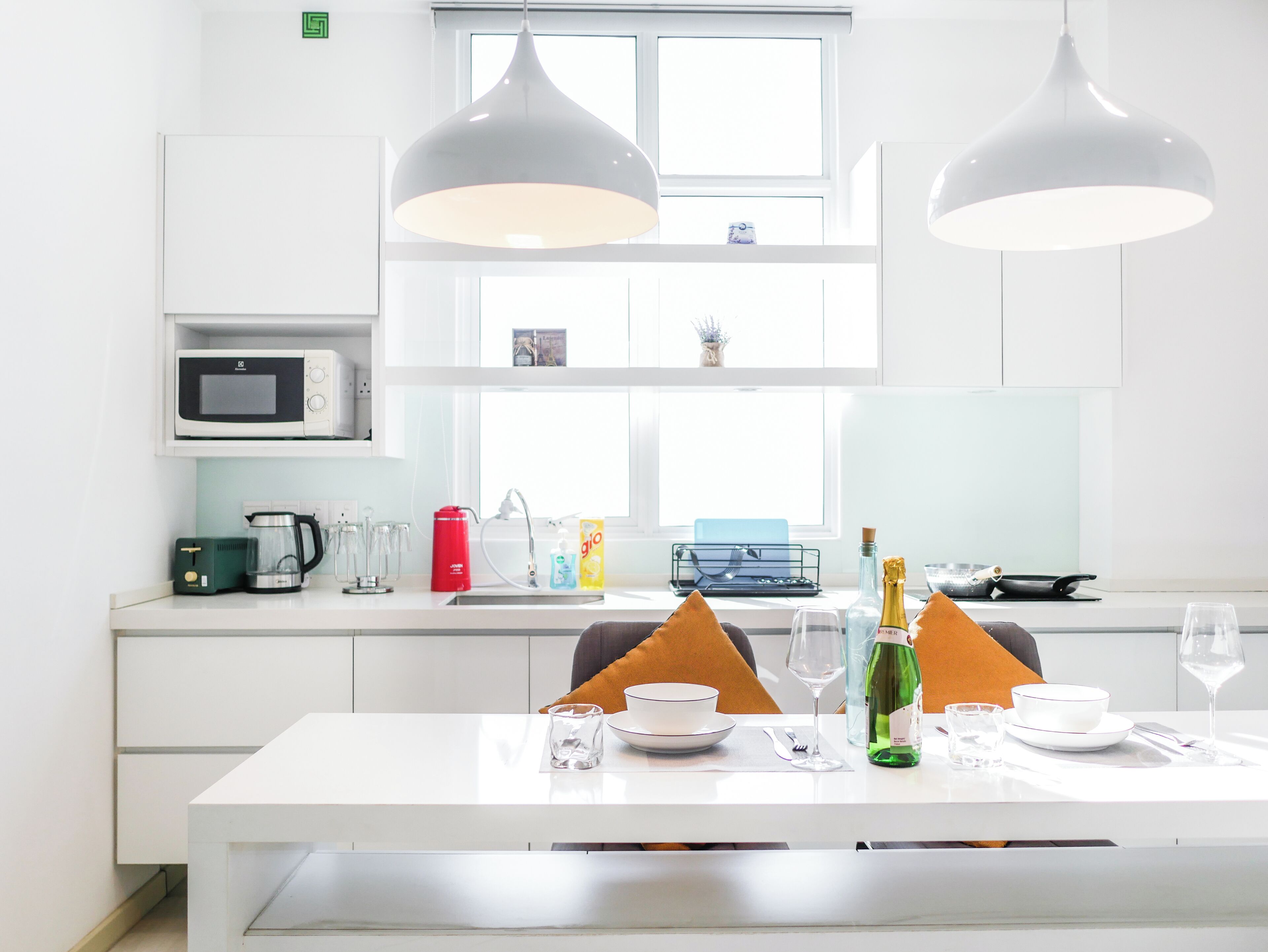A modern kitchen with white cabinetry, a microwave, a coffee maker, and a dining area with a table set for two.