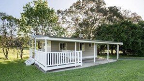 Ett envåningshus med en veranda, omgivet av en välskött gräsmatta och träd.
