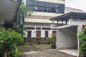 Ein Innenhof mit Blumentöpfen, einem überdachten Bereich und einem Gebäude mit großen Fenstern und einer Kachelfassade.