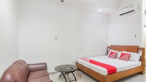 Een slaapkamer met een bed, een klein rond tafeltje, een bruine leren fauteuil en een witte muur.