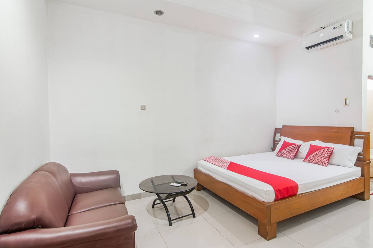 Une chambre à coucher avec un lit, une petite table ronde, un fauteuil en cuir marron et un mur blanc.