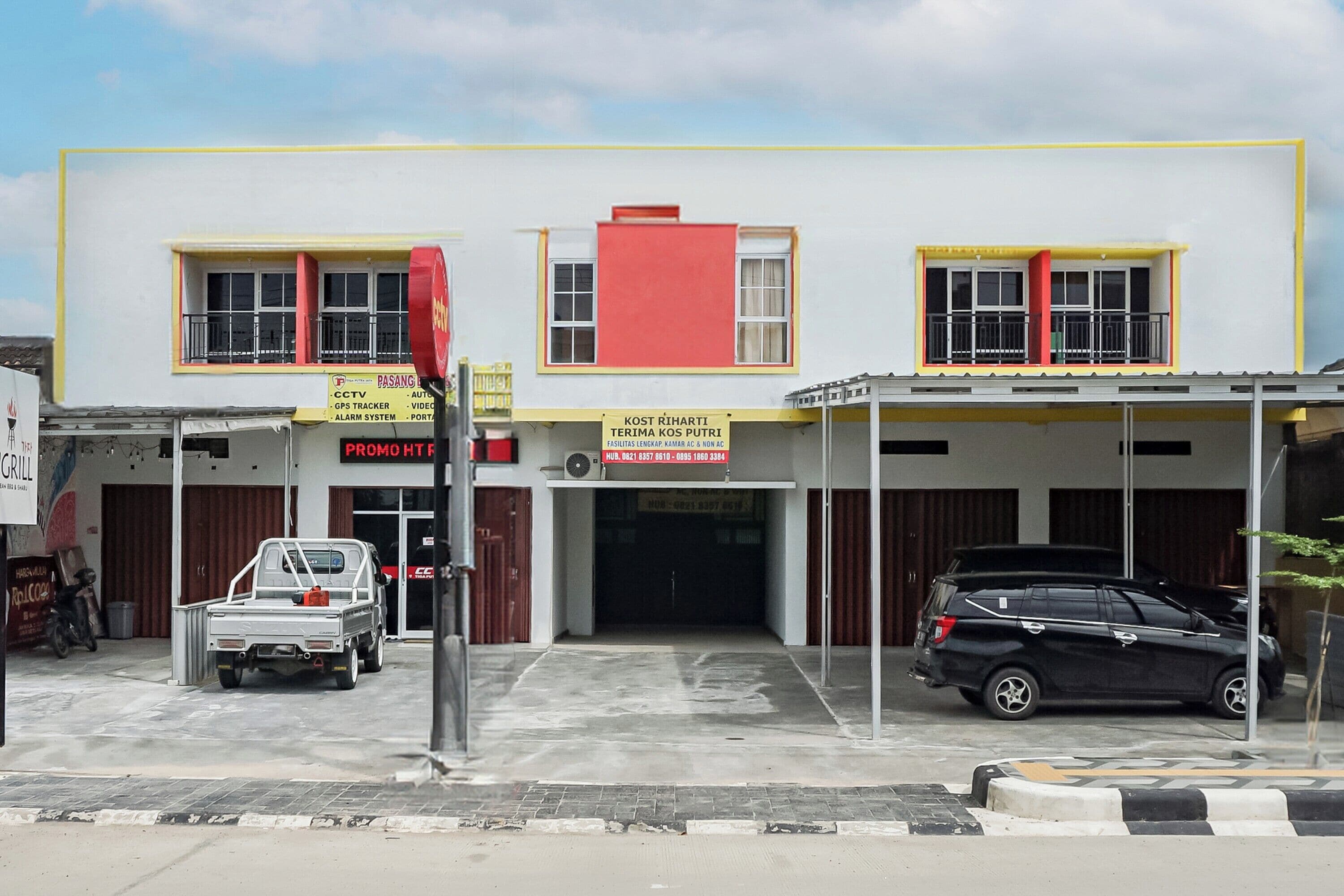 A building with a yellow and white facade, a red section on the upper floor, and a black car parked in front.