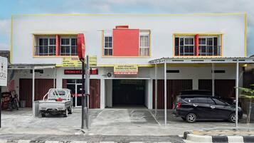 A building with a yellow and white facade, a red section on the upper floor, and a black car parked in front.