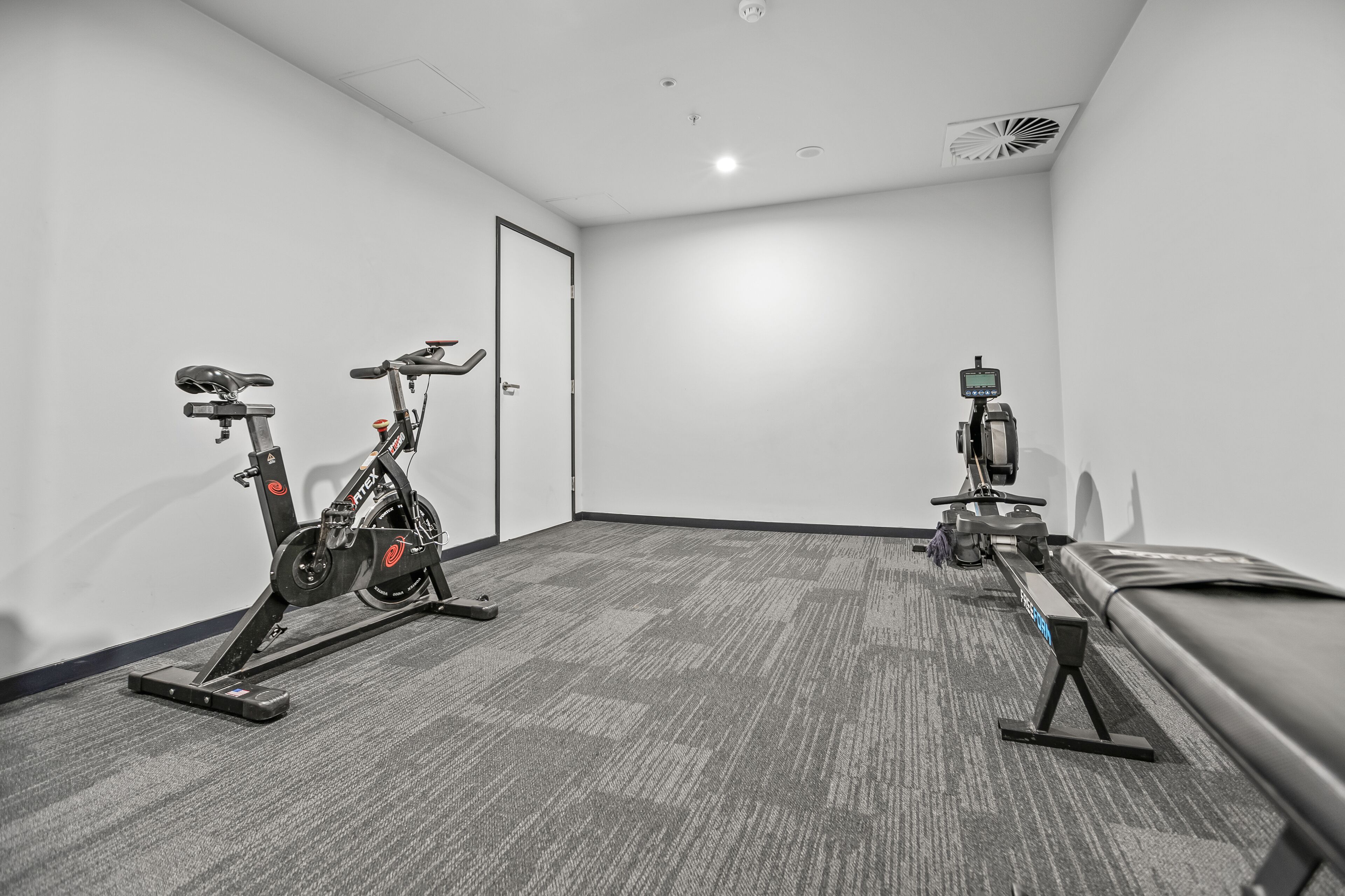A room with two stationary bikes, a bench, and a door.