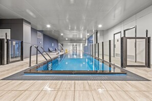 A modern indoor swimming pool with clear water, surrounded by a tiled floor and walls, and equipped with safety railings. - StayAU Modern Townhouse (Oakleigh)