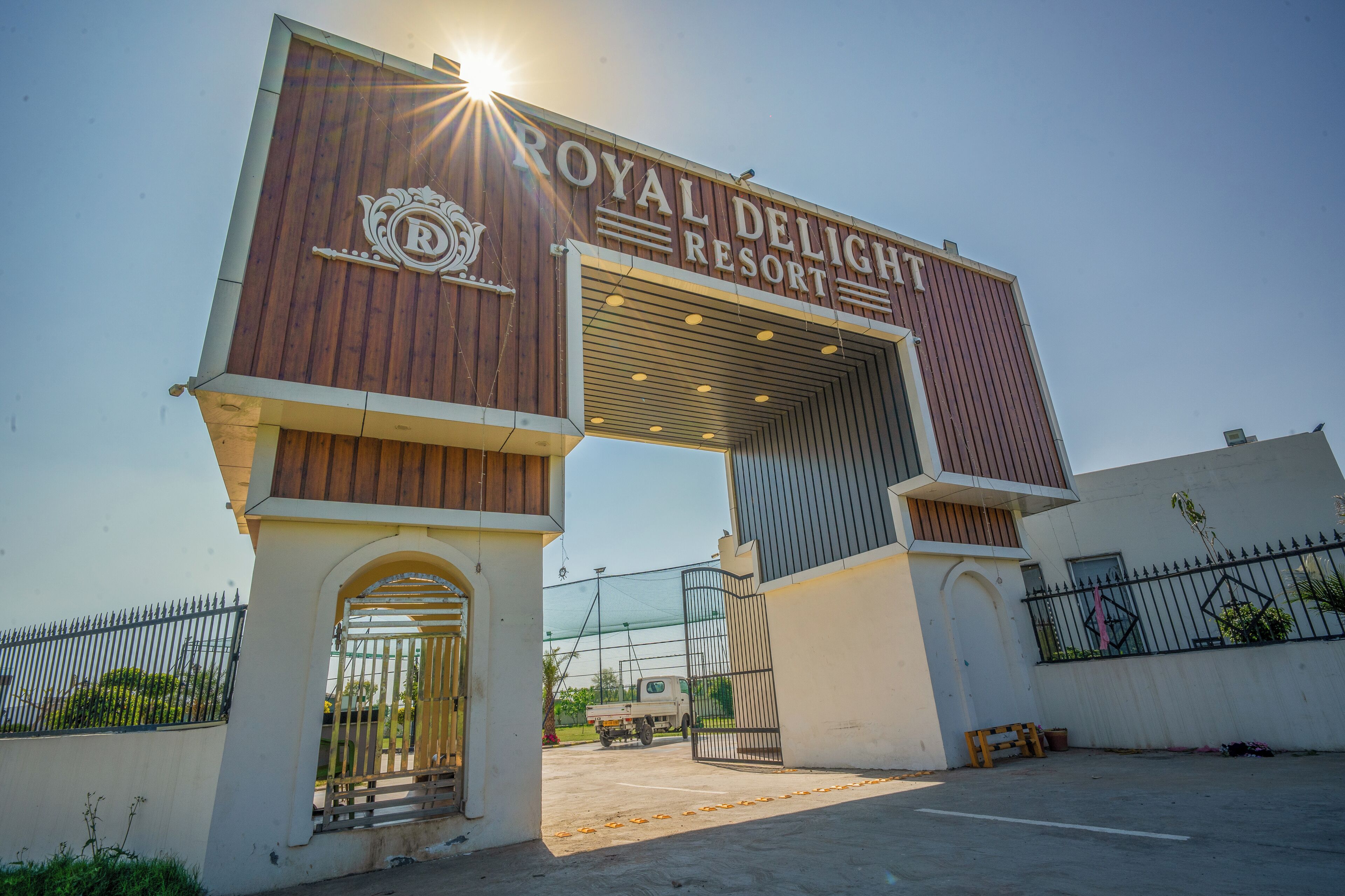 A entrada do Royal Delight Resort, com uma placa visível e um portão de acesso.