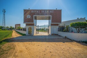 The entrance to Royal Delight Resort with a clear sky and a dirt path leading to the gate.